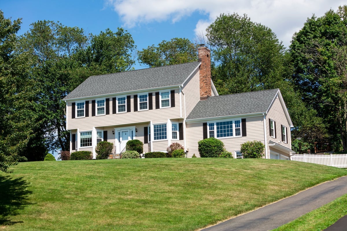 American traditional two-story Colonial home with vinyl siding, front view in summer, needs minor cosmetic work, bright daylight