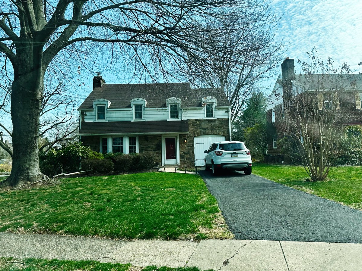 Older stone house with driveway and green lawn in a peaceful setting, mid-century home